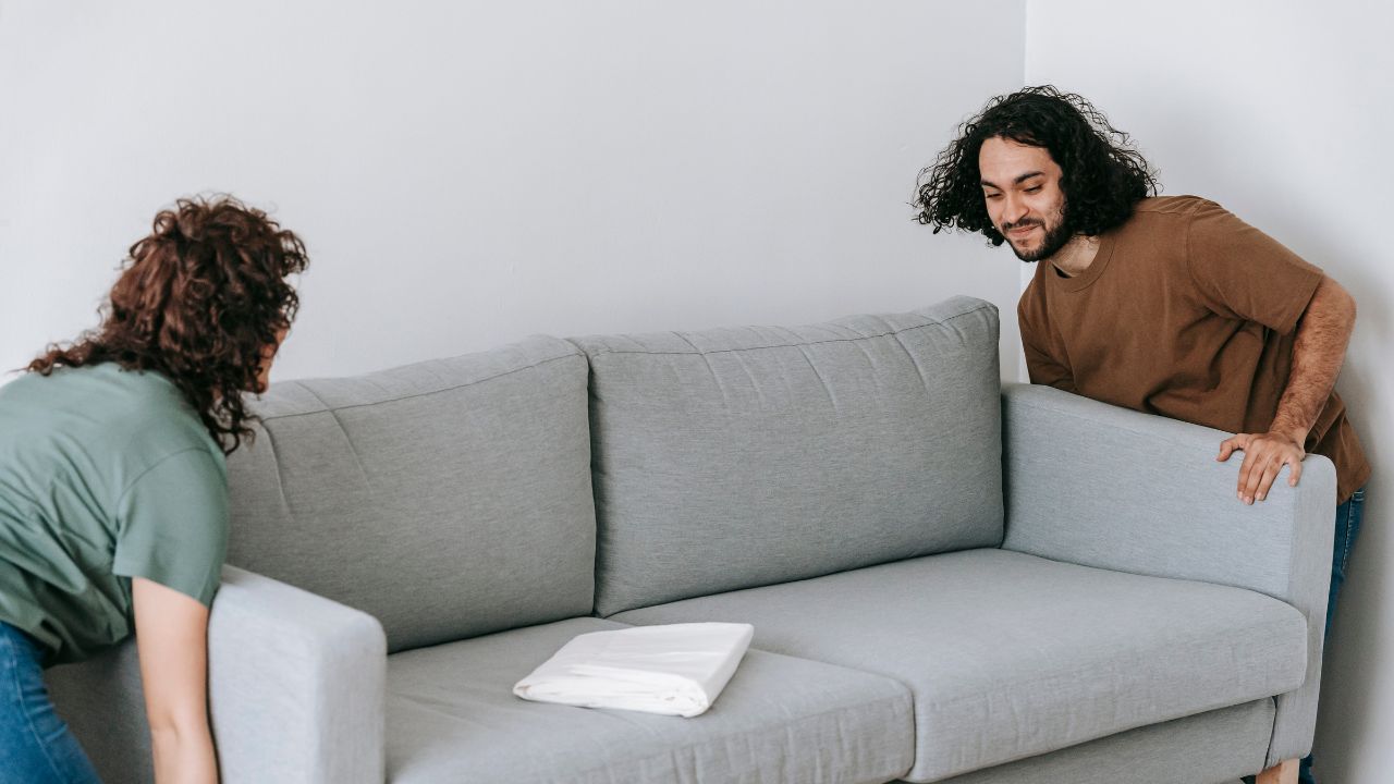 Two people moving a grey sofa